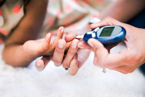 Mother is checking her daughters' diabetes by monitoring blood glucose.