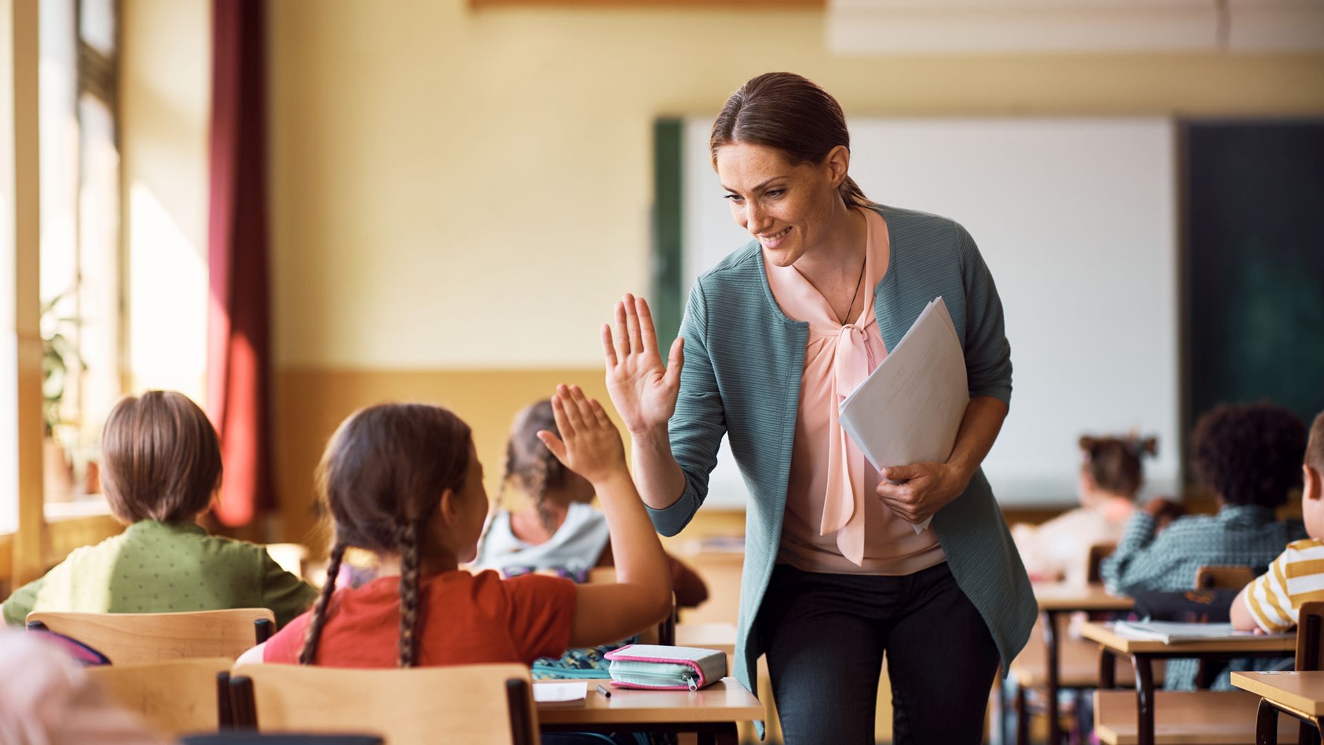 Happy teacher and schoolgirl giving high five during class at school.