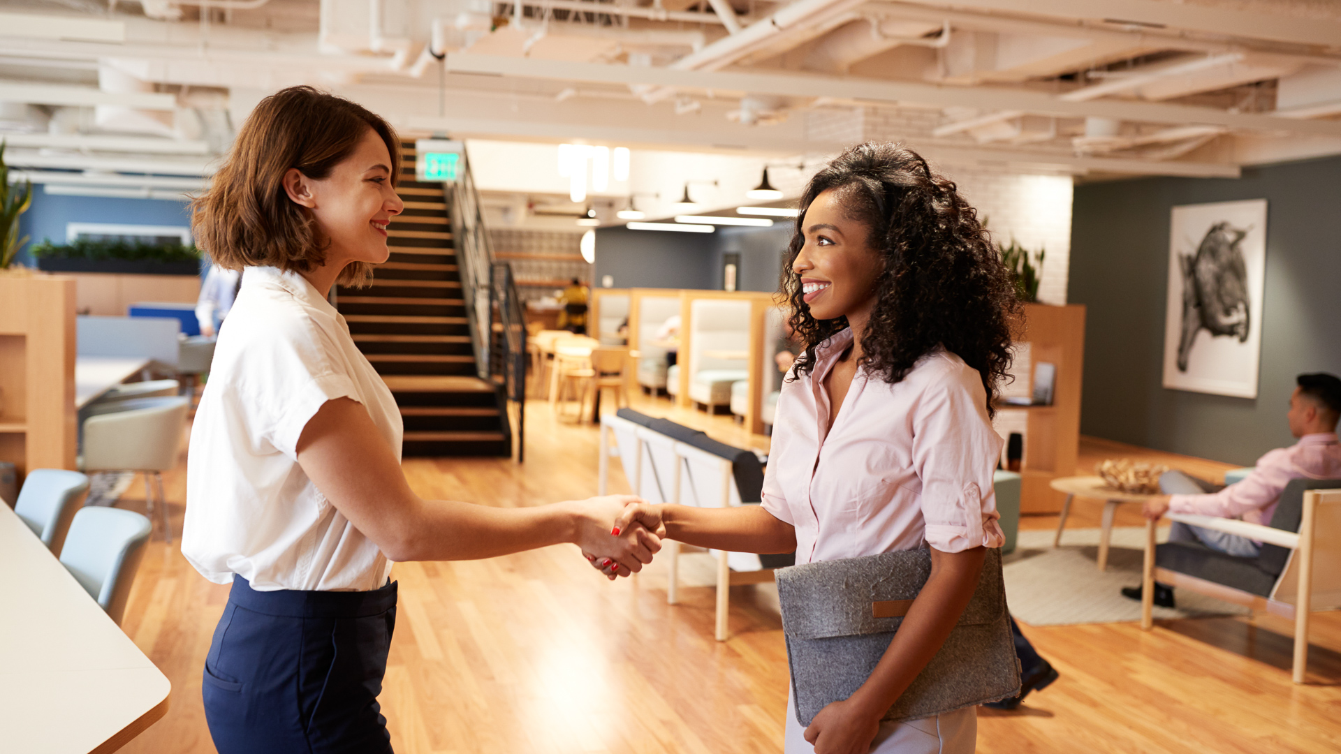Two Businesswomen Meeting And Shaking Hands In Modern Open Plan Office