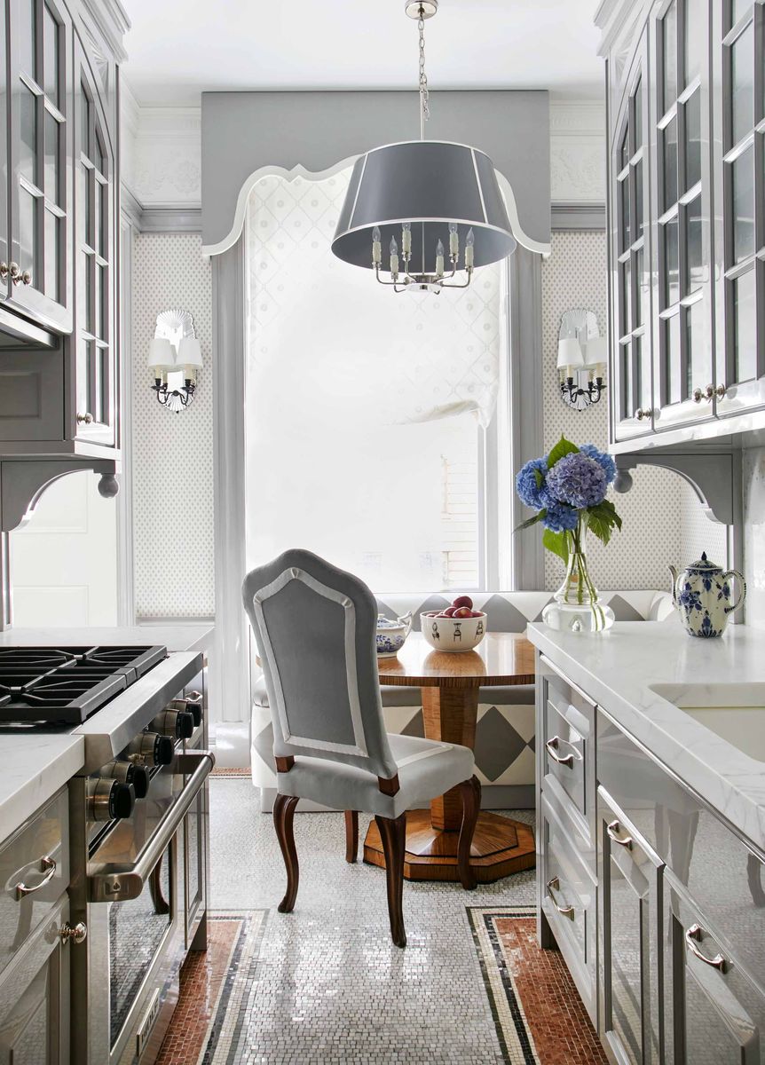 <p>In this small kitchen designed by Anthony Baratta in New York City, a theatrical pelmet and painted trim draws attention to the large window. The Apthorp’s original mosaic tile floors endure, their scale repeated in a fleur-de-lis wallpaper in the dining area. The banquette is upholstered in “1940s glam” diamond-patterned leathers (<a href="https://dualoy.com/">Dualoy</a>). The table is a Biedermeier reproduction commissioned by <a href="https://www.anthonybaratta.com/">Baratta</a>.</p>