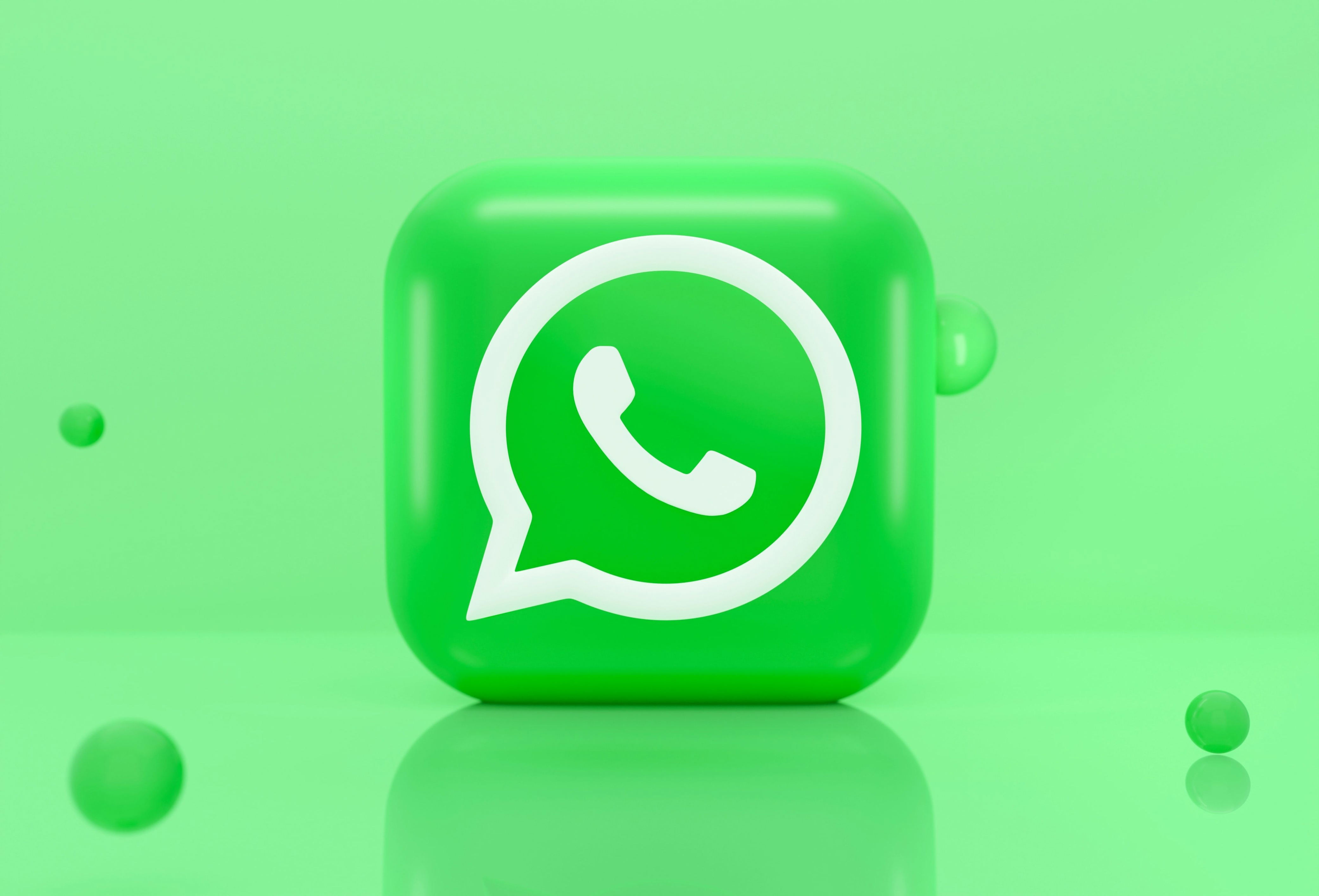  A 3D illustration of the WhatsApp logo on a green background with the reflection of the logo on the surface.
