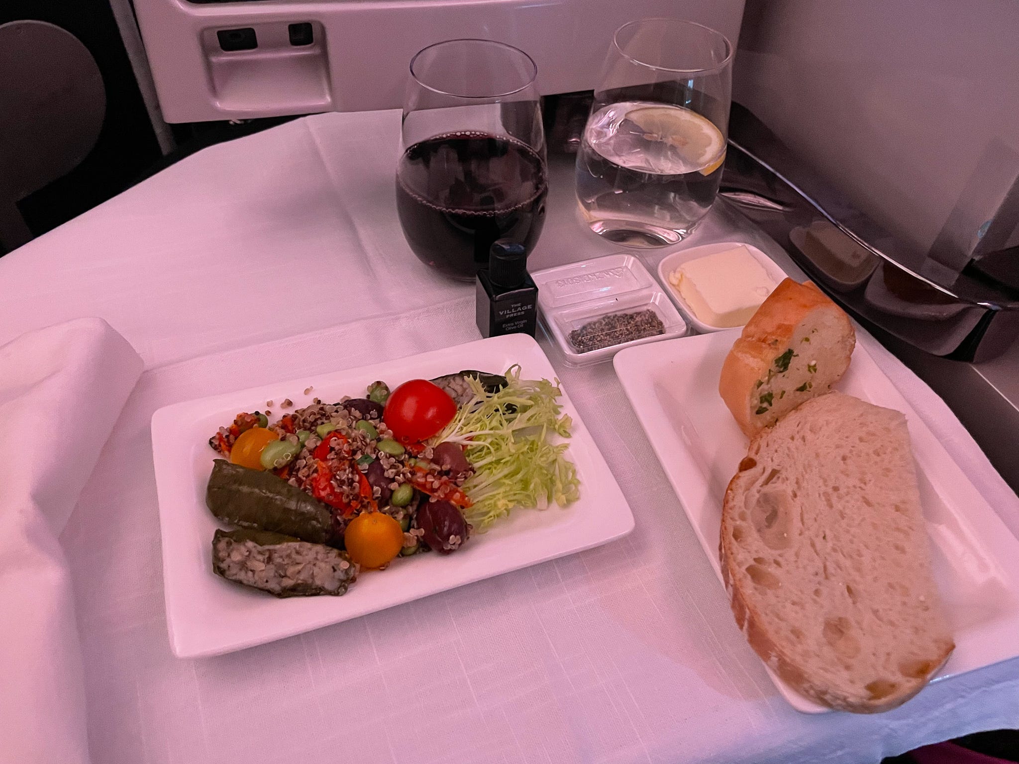 <p>When it was time to eat dinner, my first meal of the flight, a menu was provided at my seat outlining options for the three-course meal inspired by New Zealand ingredients. Beetroot-cured salmon, poached chicken, and chocolate truffle ice cream were listed on the menu. </p><p>The flight attendants kicked off dinner service by placing a cloth napkin across my tray table and laying down a set of metal silverware. I quickly realized that this meal was going to be nicer than any airline meal I've ever had.</p><p>On previous long-haul flights, as a vegetarian, I have been given one option handed to me on a tray. The meal was typically packaged and served with plastic cutlery.</p><p>So the silverware at my seat already established a drastic difference. Next, I was offered butter, olive oil, and salt and pepper. Following the condiments, the flight attendants walked around with a basket of warm sourdough and garlic bread. </p><p>Then, the first course arrived. I opted for a pescetarian meal, so I was served stuffed olive leaves. This was followed by a main course of Alaskan cod with saffron sauce, and finished with a chocolate tart for dessert. </p><p>The meal was rich and filling. From its appearance and taste, I thought the meal could easily be served in a nice restaurant rather than an airplane cabin.</p>