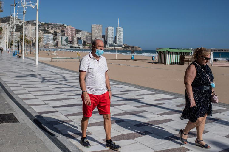 A man wearing a face mask walks along the promenade of Playa de Levante Beach