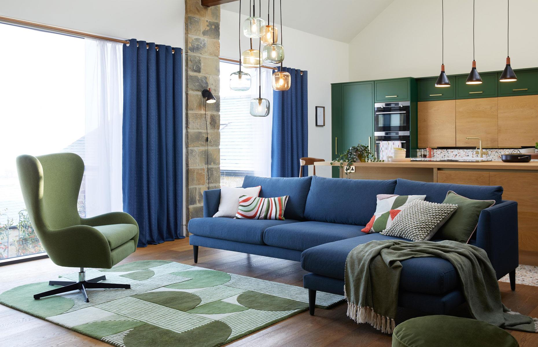 <p>In a smaller open-plan space such as an apartment use the same colors throughout to keep the room organized and unified. Here, green modern forest green kitchen cabinetry is linked to the living space by green soft furnishings. A striking blue couch blends with matching blue curtains on both the living room and kitchen windows.</p>