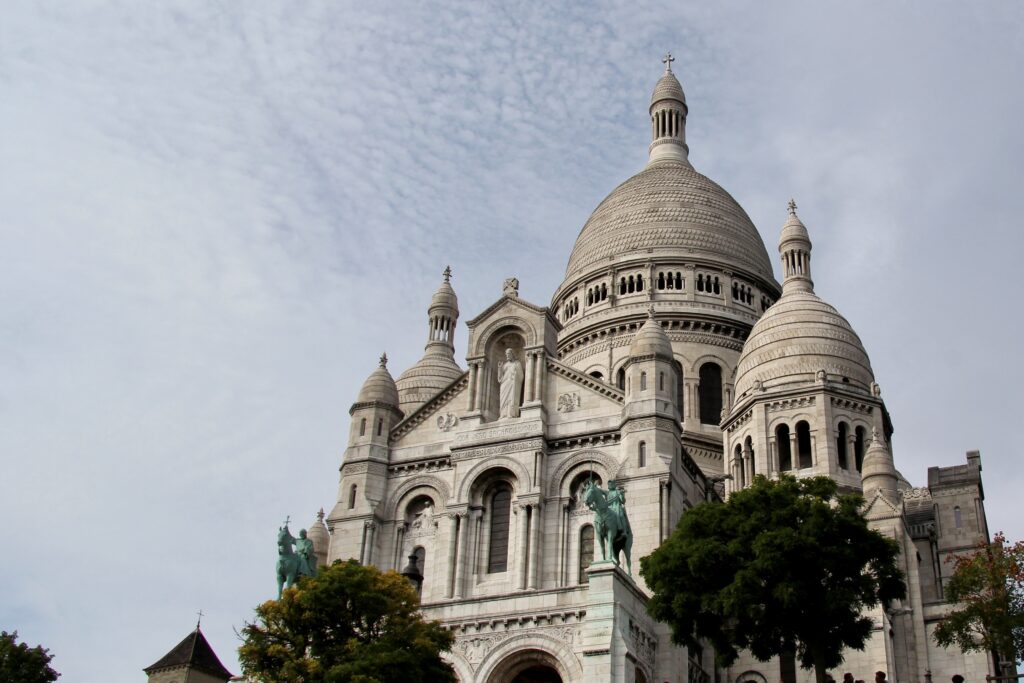 <p><em>By Martha of May Cause Wanderlust</em></p> <p>After the Eiffel Tower, one of the most prominent landmarks <a href="https://wanderwithalex.com/things-to-do-in-paris-france/">in Paris</a> is the Sacré-Cœur, or, to use its full name, The Basilica of Sacré Coeur de Montmartre. This Roman Catholic church sits on the hill of Montmartre and can be seen from all over Paris, its elongated white domes reaching heavenwards.</p> <p>The elegant Neo-Byzantine-Romanesque basilica was completed in 1914, but was not universally popular at first. You see, Montmartre was the site of the Paris Commune, a revolutionary government that briefly seized power in 1871 and resulted in thousands of Communards being executed.  Left-leaning commentators complained that the building of the church was intended to obscure the memory of the Commune.</p> <p>Visiting Sacré-Cœur is one of the best things to do in Paris, the kind of thing you should do on your <a href="https://maycausewanderlust.com/paris-first-time/" rel="noopener">first-time visit to Paris</a>. You can admire it from the gardens on the hillside below, enjoy the view from the terrace directly outside it, and you can also explore the interior.  If you don't mind a little exertion, you can also climb the 300 steps to the domes, where there's a really unique view of Paris all the way to the Eiffel Tower.</p> <p>And afterwards, have a wander around the cobbled streets of Montmartre, including the buzzing square, Place du Tertre. </p>