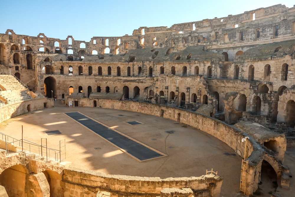 <p><em>By Kami of My Wanderlust</em></p> <p>Located in the city of El Jem in central Tunisia, the marvelous amphitheater is one of the biggest attractions of the country and one of the best-preserved Roman remnants you will ever see. This impressive structure, built around 238 AD, was in fact the third-largest amphitheater of the Roman Empire after the Colosseum of Rome and the Roman Amphitheater of Capua. </p> <p>Since 1979 the site was listed as part of the UNESCO World Heritage List. Back in its glory times, the ellipse-shaped amphitheater could fit up to 35.000 spectators, making it one of the largest buildings of that kind in the world. Today you can visit the spectacular El Jem amphitheater and explore all its corners (including the underground parts). </p> <p>The site is in really good condition (it’s better preserved than Rome Colosseum) and there are usually hardly any people around so visiting the place is very pleasant. The amphitheater is located only a 5 minutes walk from the El Jem train station, making it a very easy and accessible point in every <a href="https://www.mywanderlust.pl/tunisia-itinerary/" rel="noreferrer noopener">Tunisia itinerary</a>. </p>