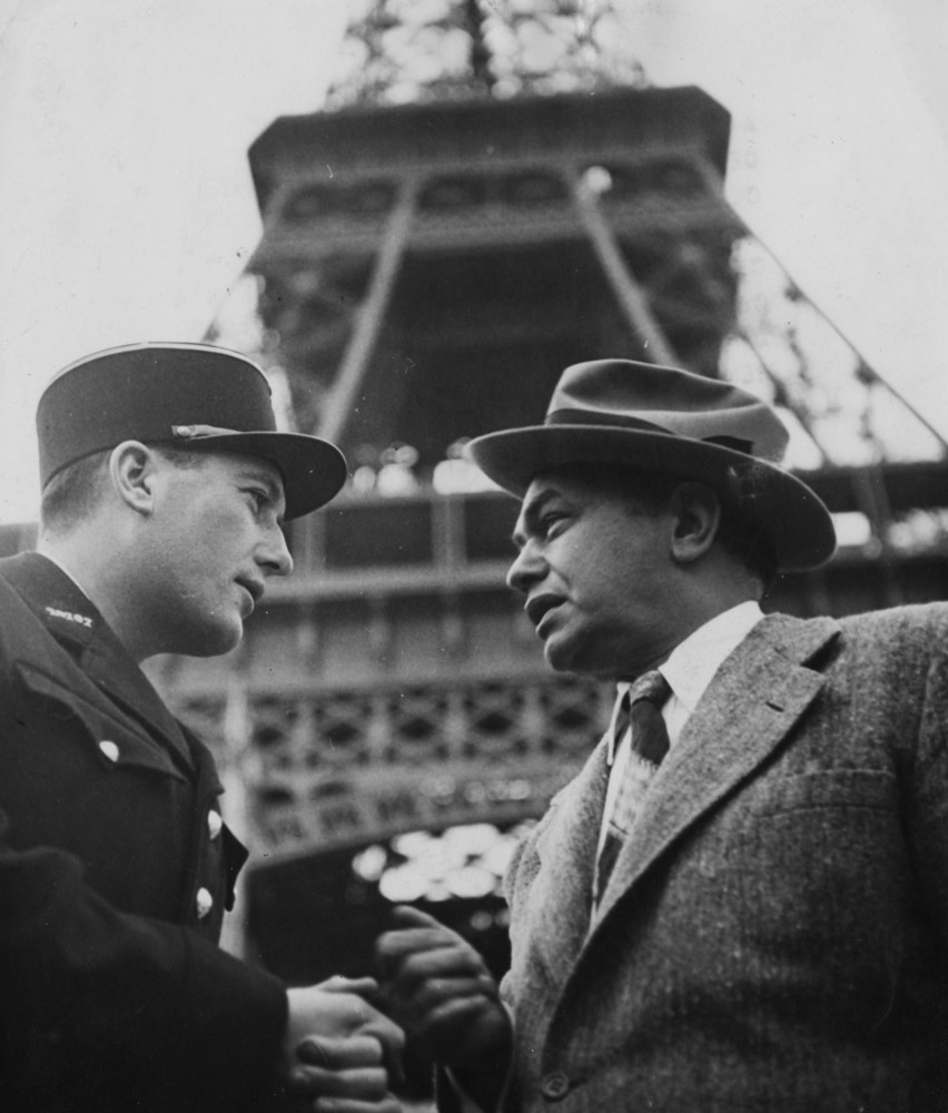 Connu pour ses rôles de gaillards, Edward G. Robinson bavarde avec un policier au pied de la tour Eiffel. Il s'apprête alors à se produire dans le spectacle "La grande nuit de Paris" en faveur de l'association "International Children's Fund, circa", vers 1950.