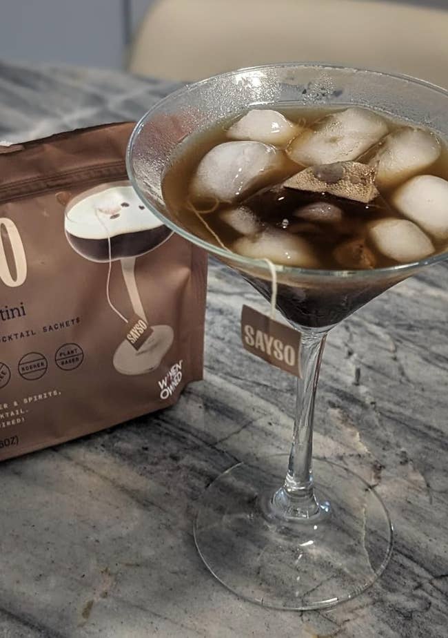 Martini in a glass with ice next to a package of cocktail sachets on a marble surface