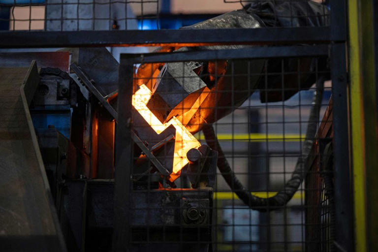 Ein grauer Roboterarm bewegt einen geschmolzenen Stahlknüppel während des Herstellungsprozesses von 155 mm Artilleriegeschossen in einer europäischen Fabrik.