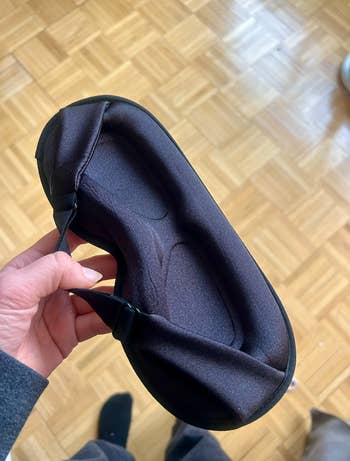 A hand holds a padded black sleep mask, perfect for comfortable rest and blocking light. Suitable for enhancing sleep quality