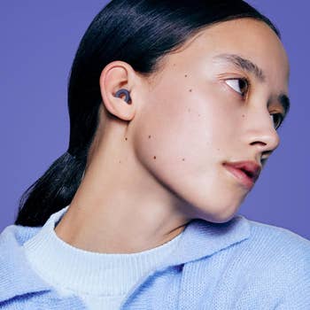 Person with sleek hair models wireless earbuds, wearing a cozy sweater, looking off to the side