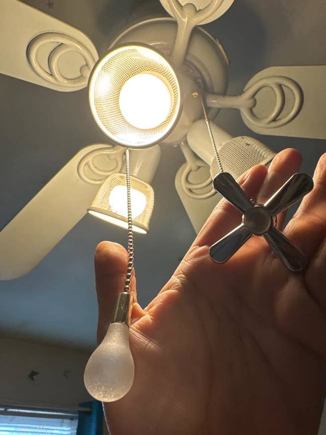 Hand pulls ceiling fan chain with light bulb and fan blade design