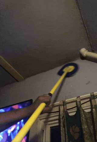 Someone is using a yellow mop to clean a ceiling near pipes in a room