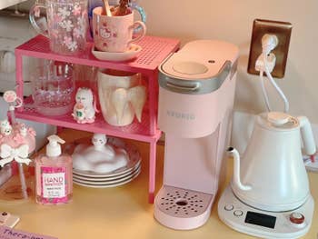 Coffee station with a pink Keurig, white electric kettle, mugs, and hand sanitizer
