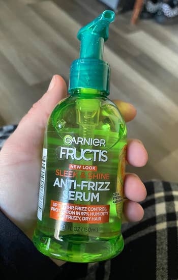 Hand holding Garnier Fructis Sleek & Shine Anti-Frizz Serum bottle, promising 97% humidity protection and frizz control for dry hair