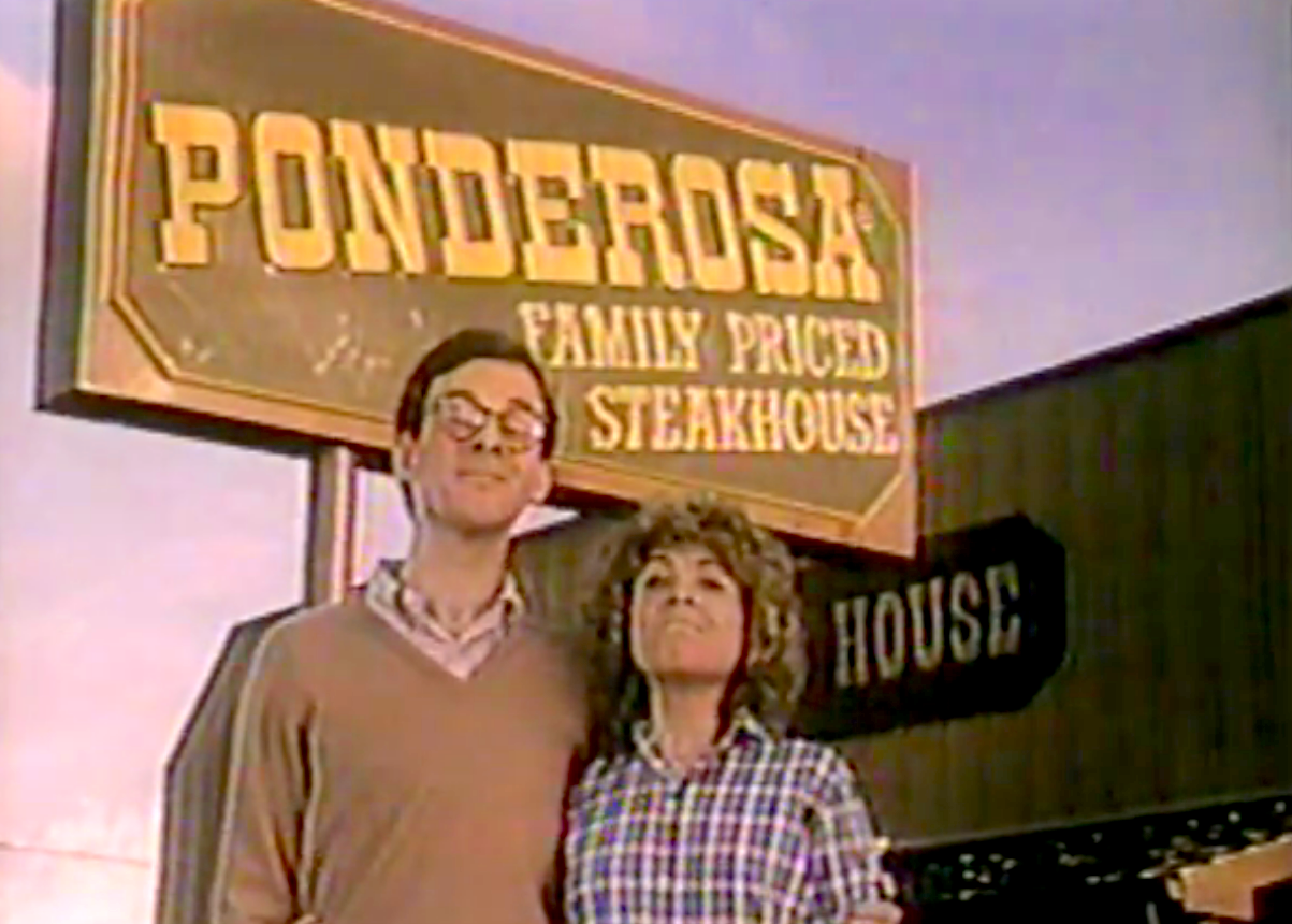 Two people stand in front of a Ponderosa Family Priced Steakhouse sign