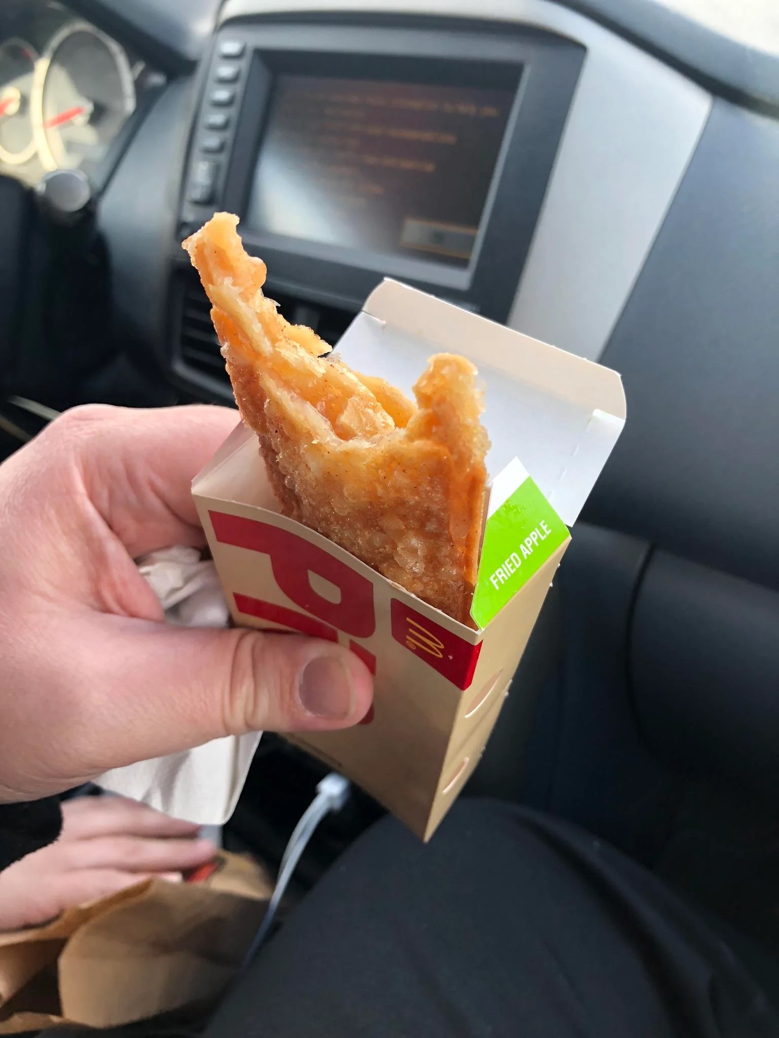A person holds a McDonald's fried apple pie inside a car, showcasing the crispy dessert in its packaging