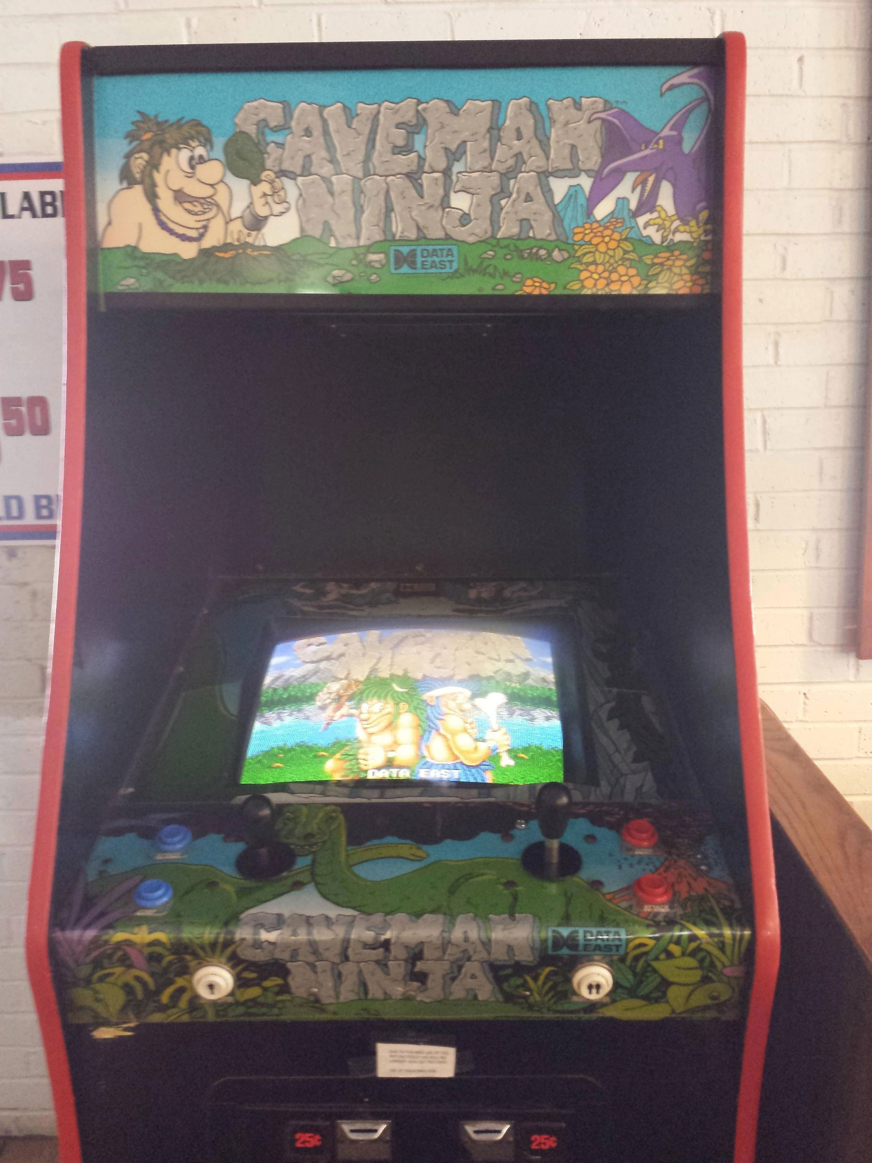 Arcade machine featuring the game "Caveman Ninja" with colorful graphics displayed on the screen, set in a playful prehistoric theme