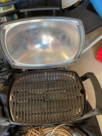 A portable indoor grill with a clean lid and used grill grates, surrounded by various household items