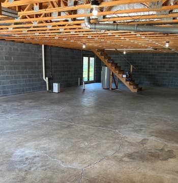 Unfinished basement with concrete floor, exposed beams, wooden staircase, and visible utilities. Potential space for home improvement projects