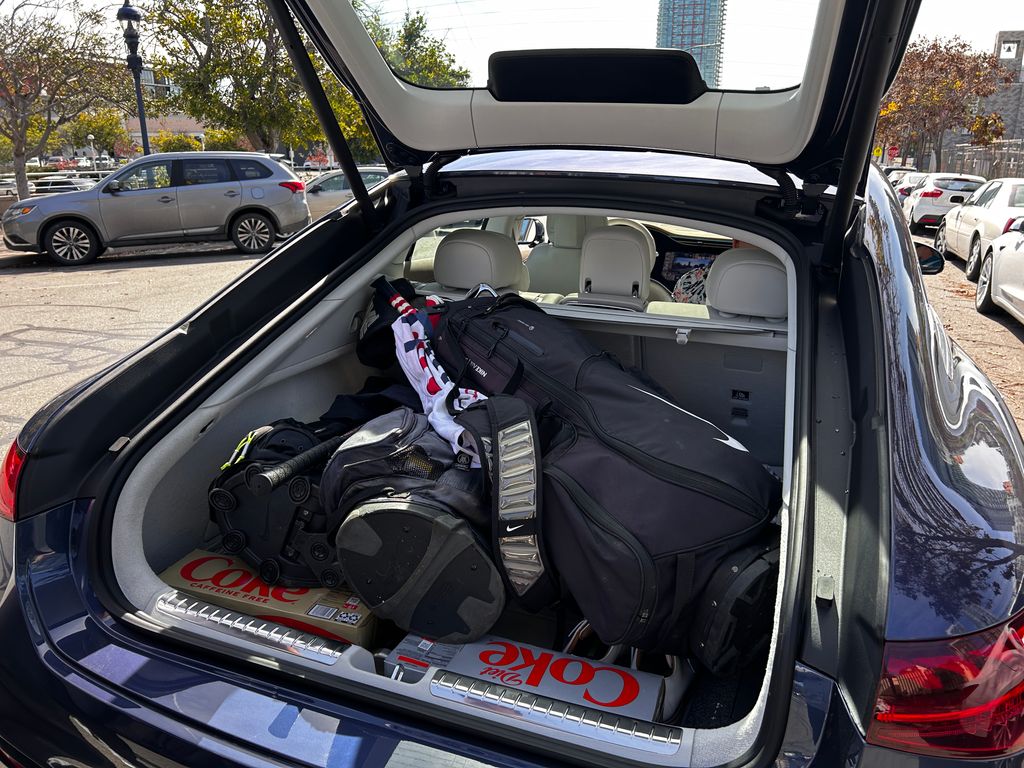 A Mercedes EQS with three bags of golf clubs in the trunk.