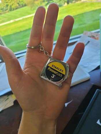 Hand holding a keychain shaped like a Stanley PowerLock 3-foot tape measure