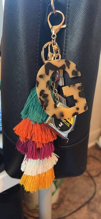 Leopard print initial keychain with colorful tassels hangs on a black bag