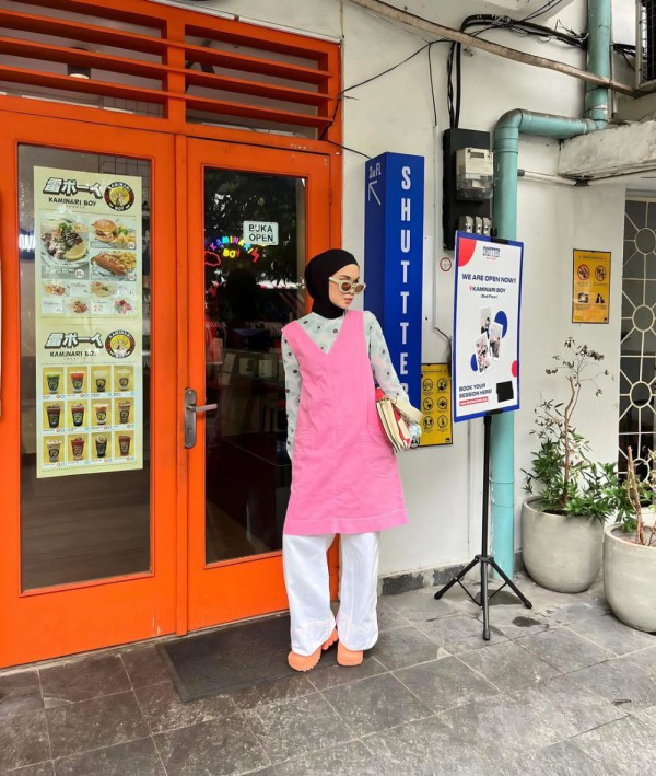 Kemeja bergaris putih retak, gaun midi berwarna pink secara keseluruhan, celana putih, serta jilbab berwarna hitam Kemeja bergaris putih retak, gaun midi berwarna pink secara keseluruhan, celana putih, serta jilbab berwarna hitam