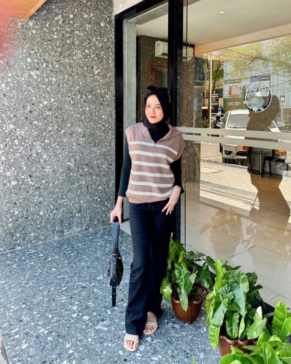 Penampilannya mencolok seperti kombinasi antara gaun dalam dan celanaflare yang semuanya berwarna hitam gelap, dipadukan dengan luaran tanpa lengan warna cokelat yang memiliki motif garis putih sebagai aksen. Penampilannya mencolok seperti kombinasi antara gaun dalam dan celanaflare yang semuanya berwarna hitam gelap, dipadukan dengan luaran tanpa lengan warna cokelat yang memiliki motif garis putih sebagai aksen.
