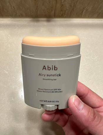 Person holding Abib Airy Sunstick, a broad-spectrum SPF 50+ smoothing bar, water-resistant for 60 minutes, net weight 0.81 oz (23g)