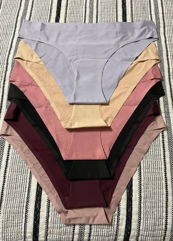 Stack of seamless women's underwear in various neutral tones, displayed on a striped fabric background