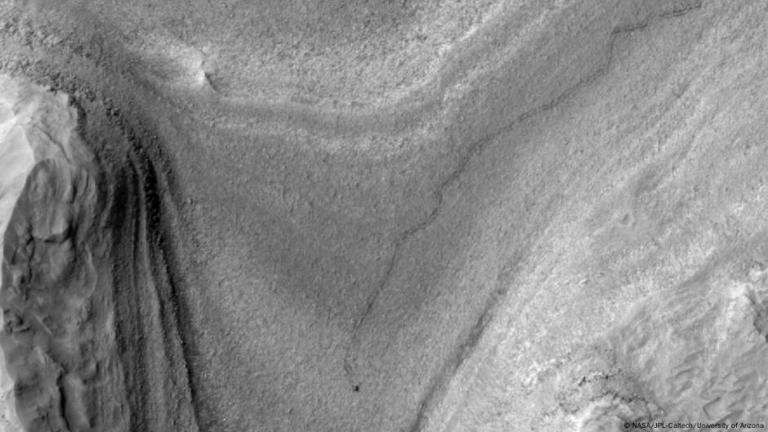La imagen muestra al rover Curiosity -punto negro inferior- en Marte, y las huellas dejadas por sus ruedas.