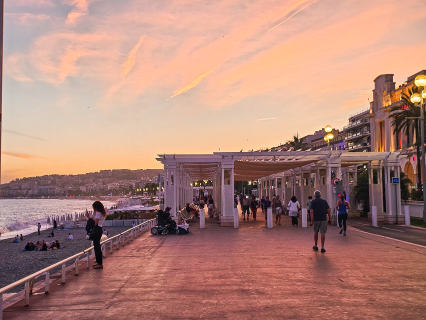 A white wood restaurant and gazebo on the beach. The sky is pink, yellow, and blue with reflections on the water.