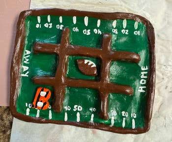 Clay football field with a tic-tac-toe design, featuring a small clay football and an orange jersey, labeled
