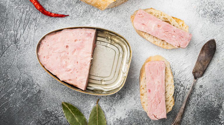 A half-full can of ham, with slices of canned ham on bread pieces