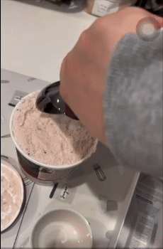 Scooping ice cream from a tub with a gray ice cream scooper on a kitchen counter