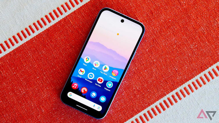 The Pixel 9a on an orange and white backdrop with the display on and facing up.