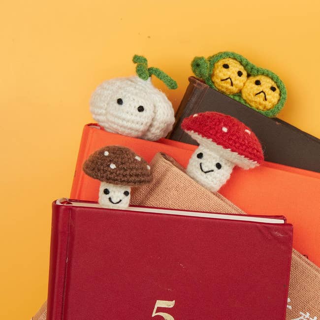 Crochet bookmarks shaped like a garlic, pea pod, and mushrooms on books. Suitable for book lovers or as gift ideas
