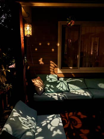 Outdoor patio with cushions shows intricate light patterns from nearby hanging lanterns creating a cozy atmosphere