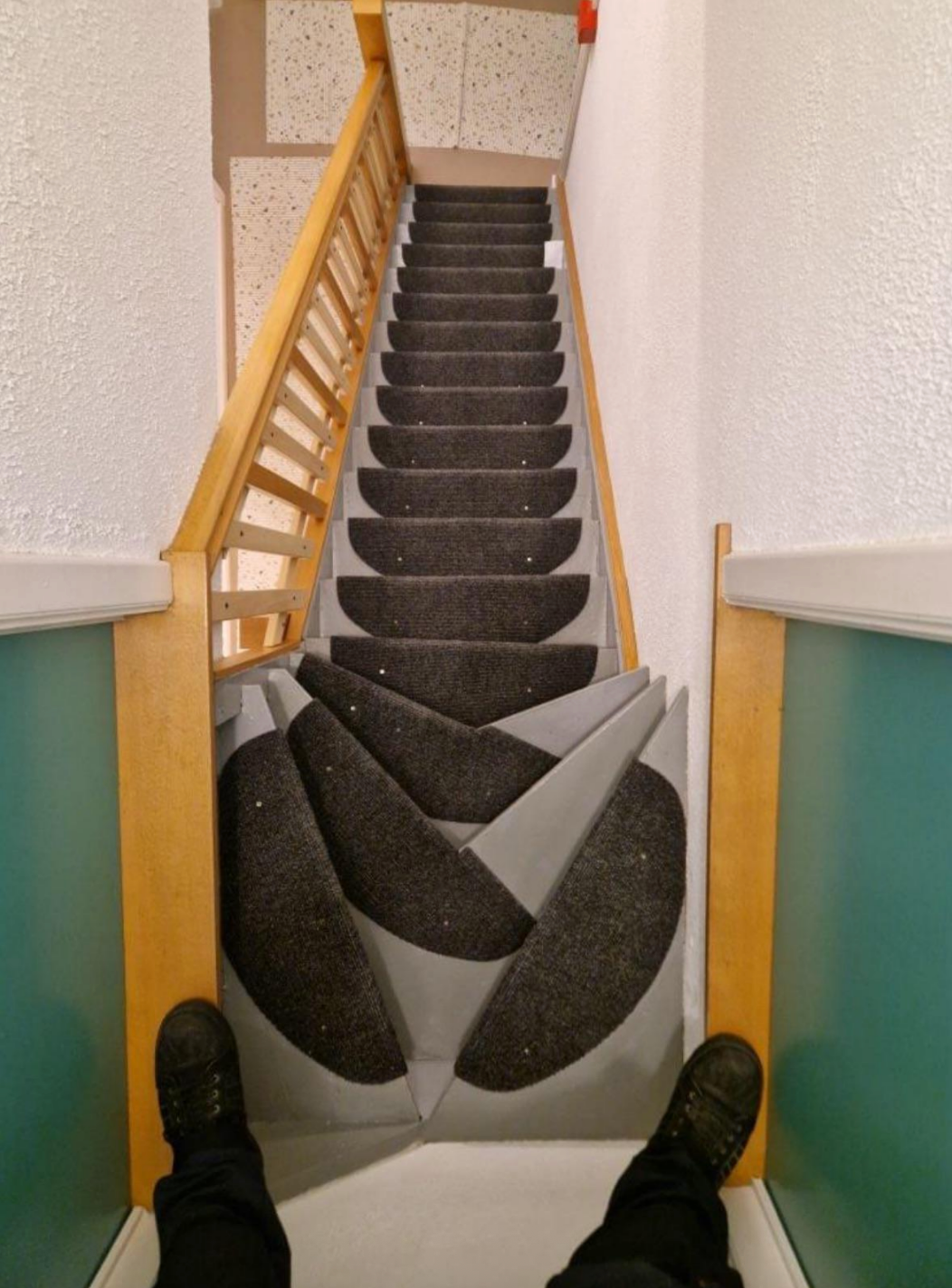 Staircase with overlapping carpet patterns, creating an optical illusion. View from above with shoes visible at the top step