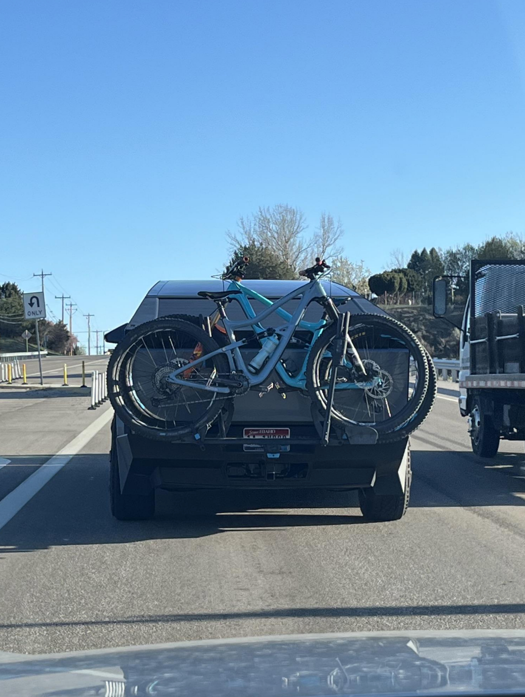 Vehicle on highway has bicycles mounted on rear bike rack. Road and trees visible in the background