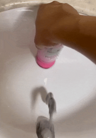 Liquid soap being dispensed into a sink from a pink bottle
