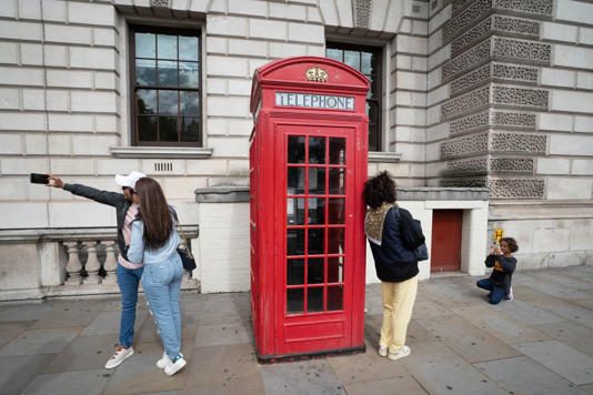 Tourists and visitors to London have their photo taken beside a red phone box at Parliament Square (PA) - PA Archive