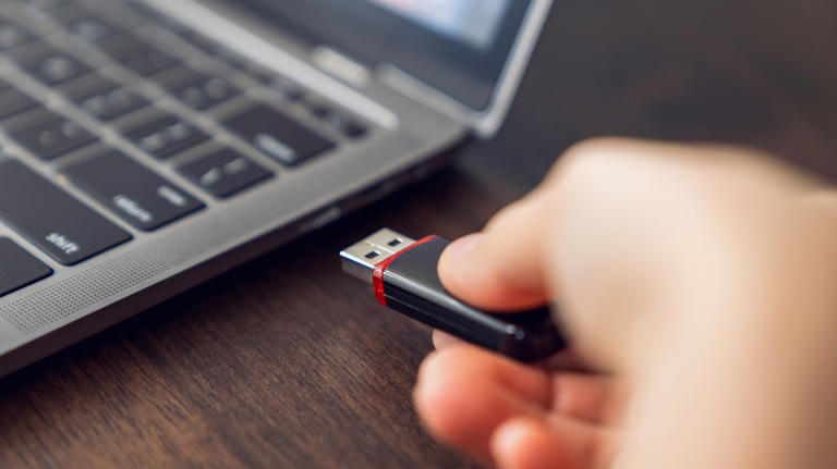 Person holding USB drive next to a computer