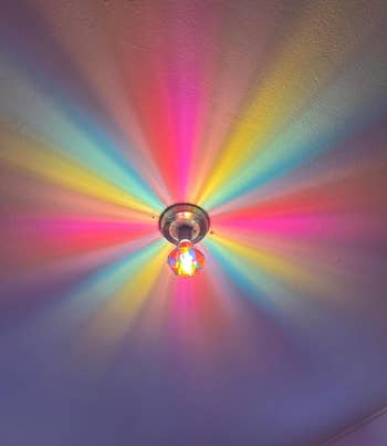 Light fixture on ceiling casts a starburst pattern of multicolored rays across the ceiling, creating a vibrant and eye-catching display