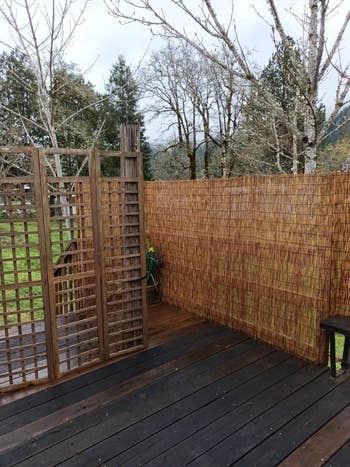 Wooden deck with privacy screens made of lattice and bamboo, overlooking trees and a grassy area