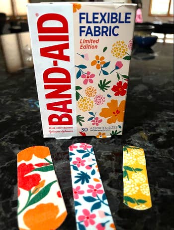 Box of limited edition BAND-AID flexible fabric with floral designs, alongside three floral-patterned bandages