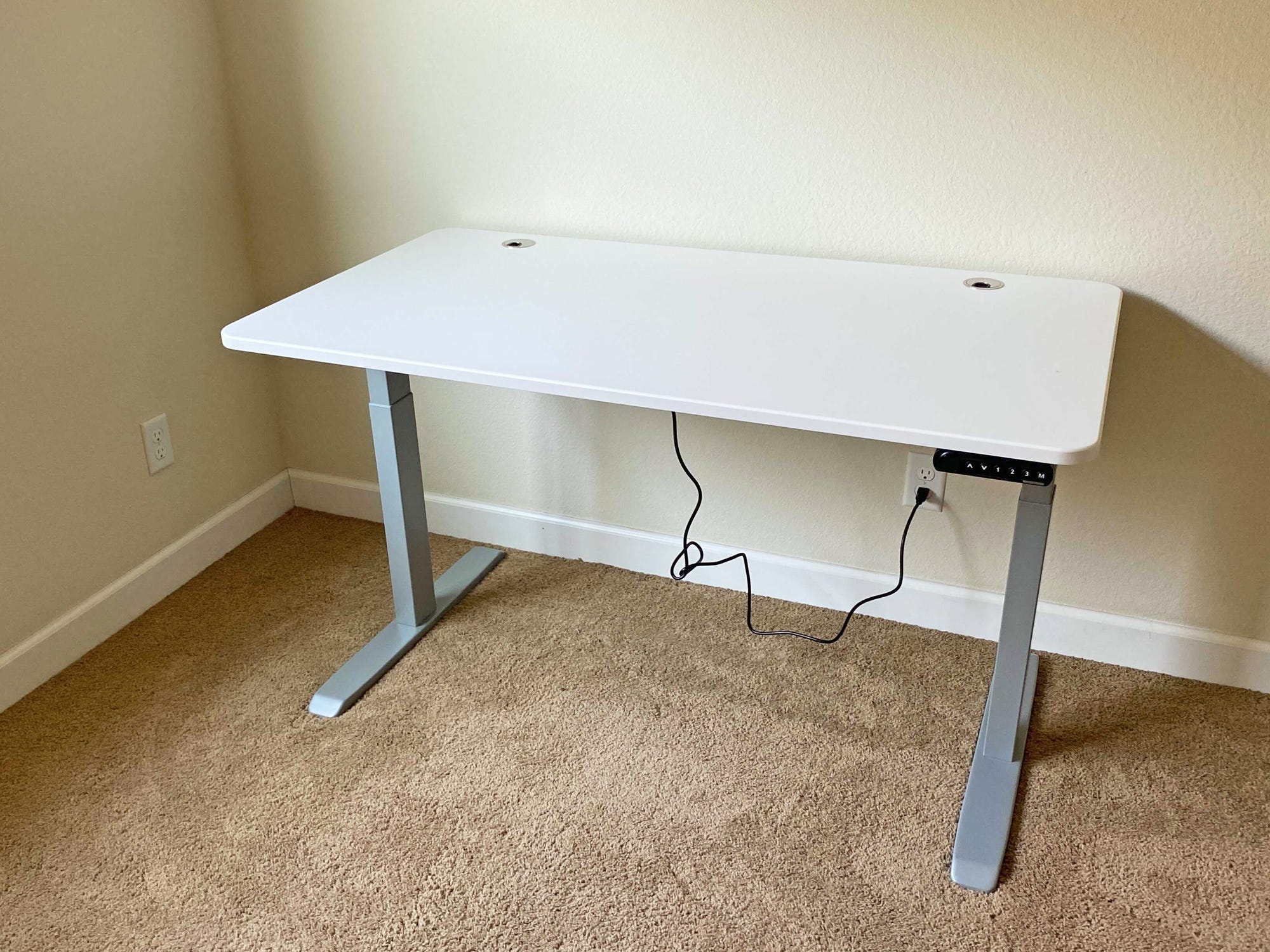 A bare white Autonomous SmartDesk Connect sits in a yellow room on a carpeted floor.