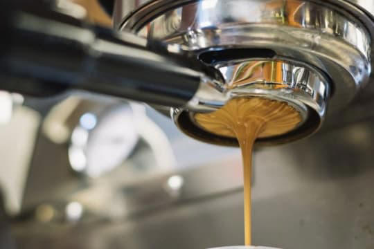 Café expreso recién salido de una máquina profesional, con el líquido fluyendo hacia una taza. La imagen representa la preparación de una dosis precisa de cafeína antes del entrenamiento, clave para mejorar el rendimiento físico y cognitivo.