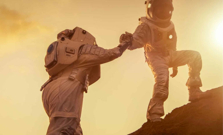 Two Astronauts Climbing A Mountain, Helping Each Other, Reach The Summit. Credit: ShutterStock | The Daily Galaxy --Great Discoveries Channel